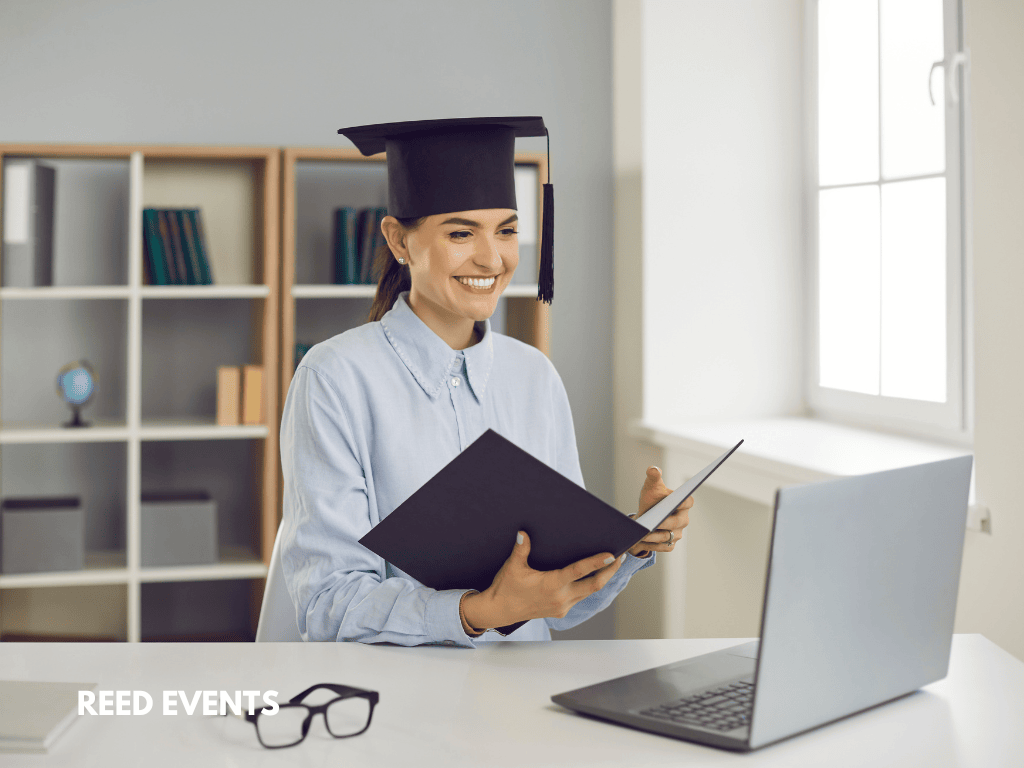 A girl wearing a graduation cap is looking at a laptop